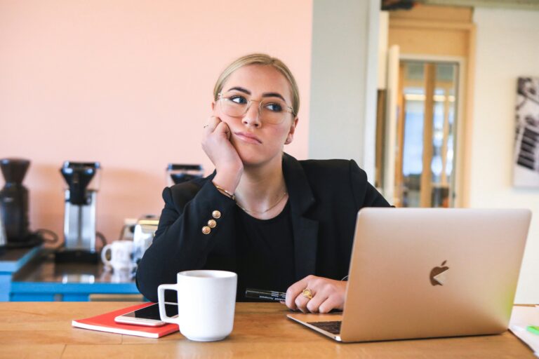 A woman looks bored, dressed in business clothes and sitting at a desk.