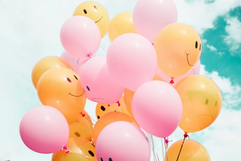 Pink and orange balloons sporting smiley faces against a sunny sky