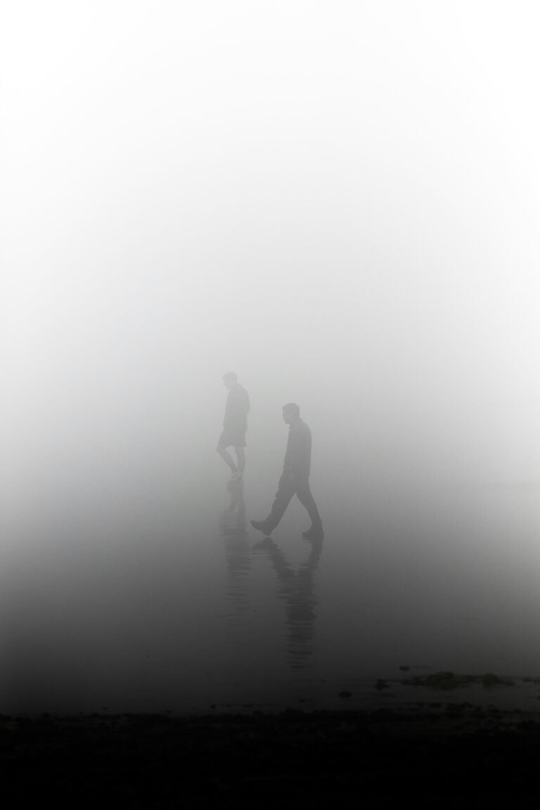 Two figures walk through a fog