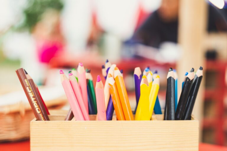 Coloured pencils in a box against a blurry childcare centre background
