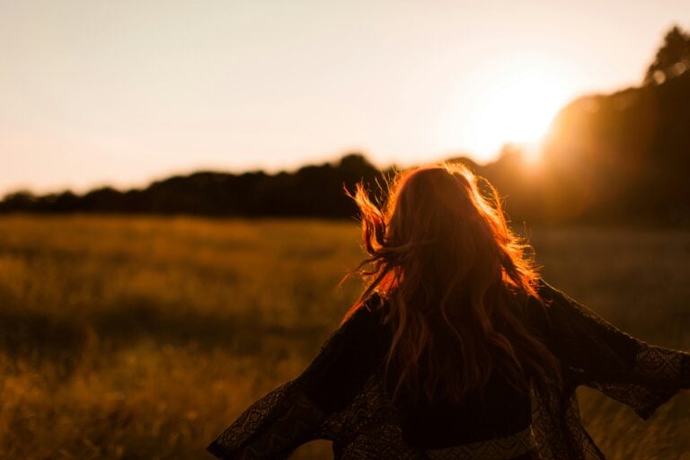 Viewed from behind, a person moves with outstretched arms through a field in the sunset light.