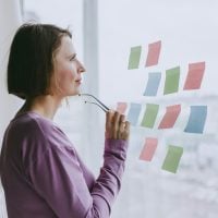 Someone stands at a window, glasses in hand. She looks at post it notes on the window.