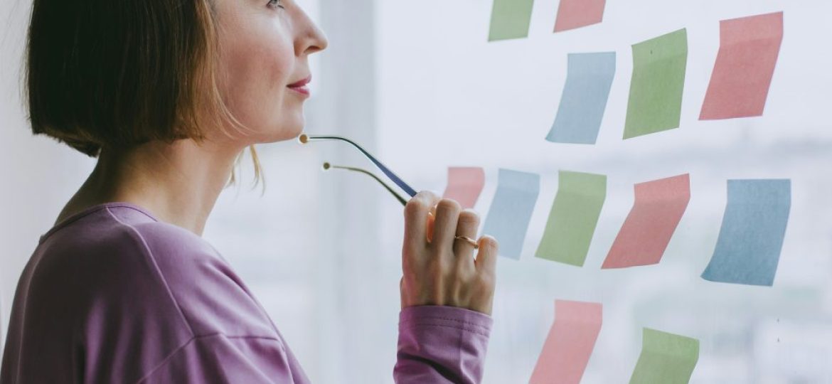 Someone stands at a window, glasses in hand. She looks at post it notes on the window.