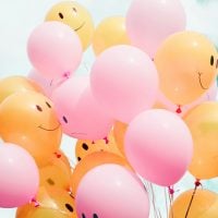 Pink and orange balloons sporting smiley faces against a sunny sky