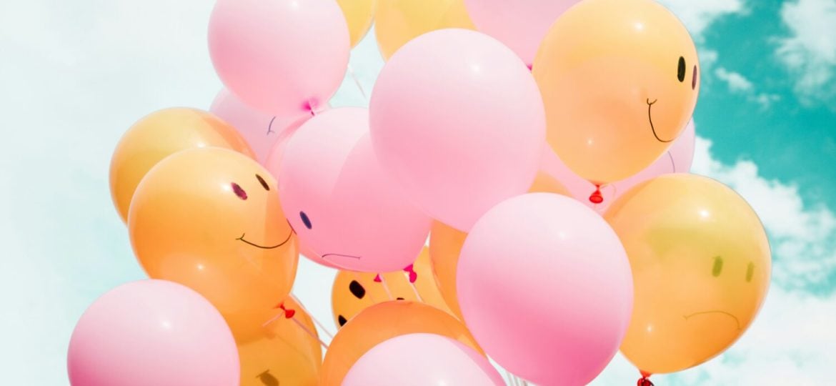 Pink and orange balloons sporting smiley faces against a sunny sky