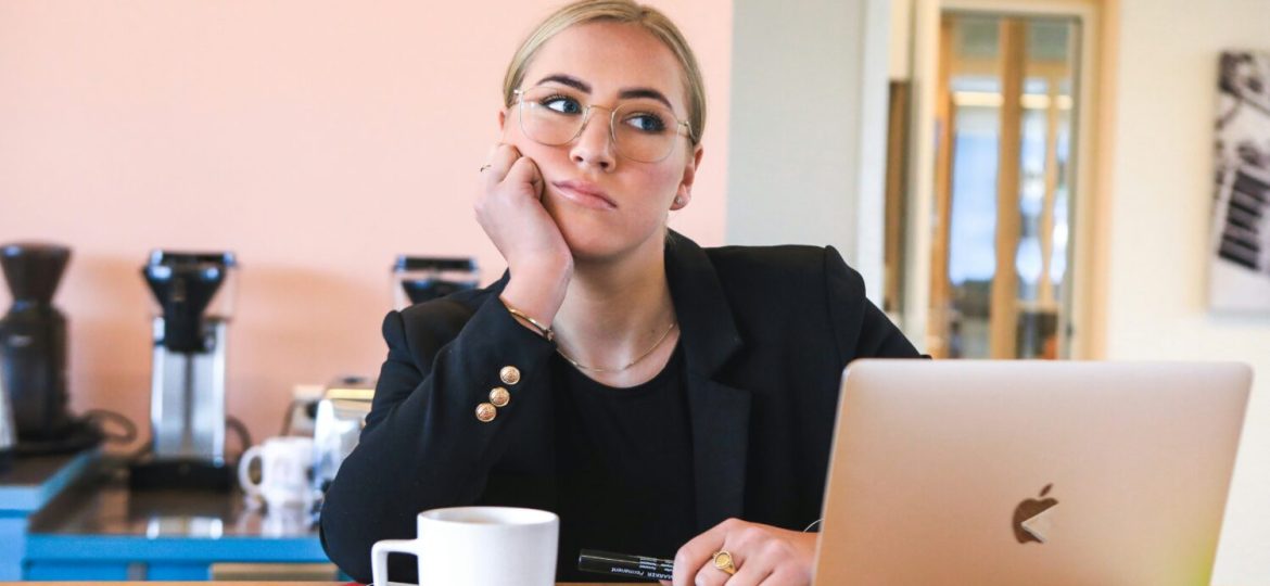 A woman looks bored, dressed in business clothes and sitting at a desk.