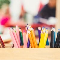 Coloured pencils in a box against a blurry childcare centre background