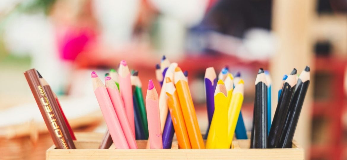 Coloured pencils in a box against a blurry childcare centre background