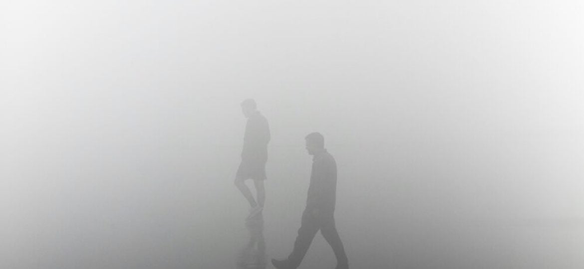 Two figures walk through a fog