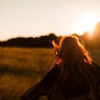 Viewed from behind, a person moves with outstretched arms through a field in the sunset light.