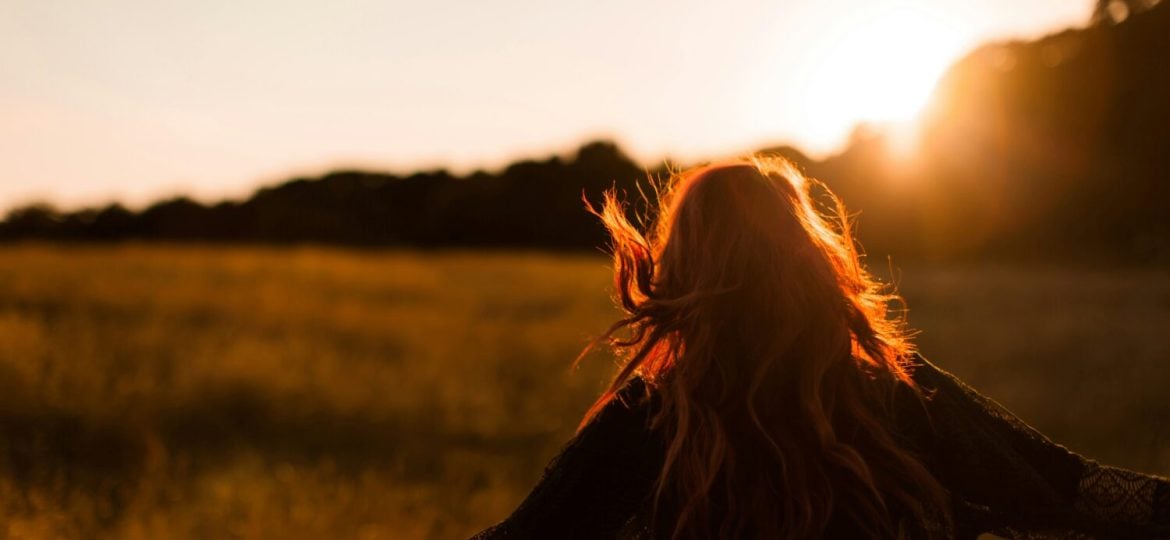 Viewed from behind, a person moves with outstretched arms through a field in the sunset light.